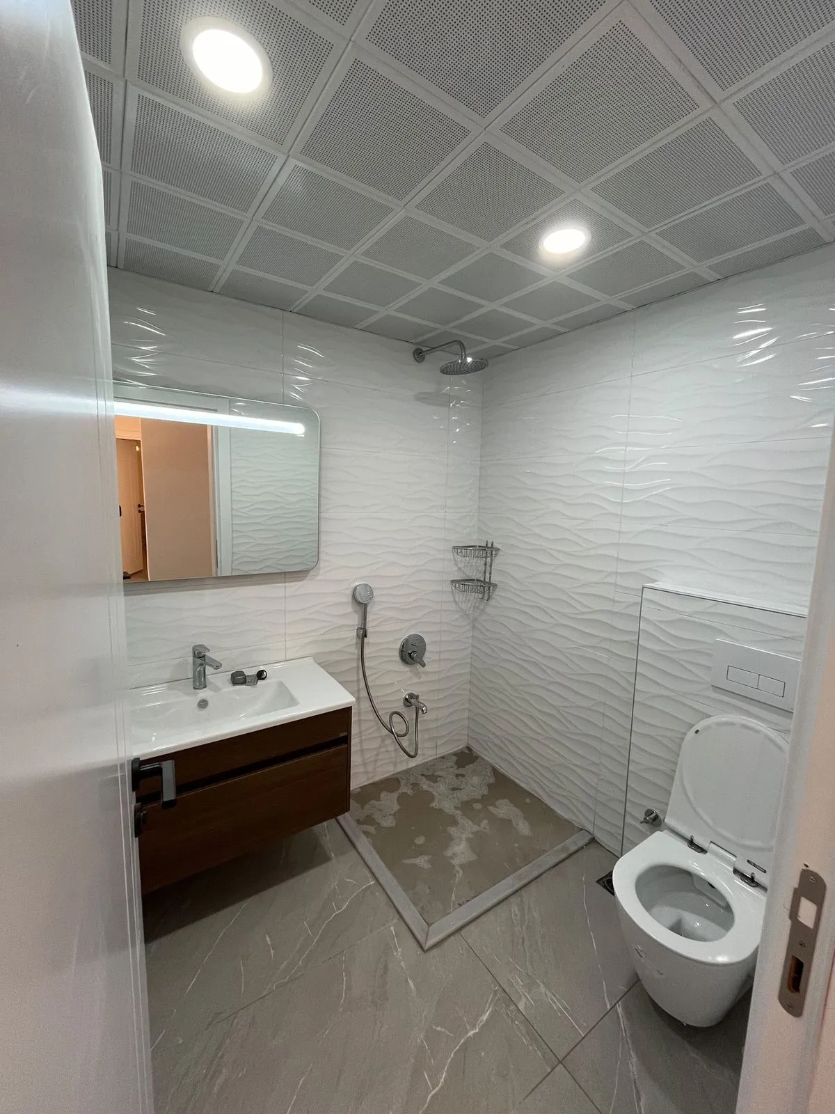 Beyaz dalgalı seramikli banyo ve ahşap lavabo dolabı